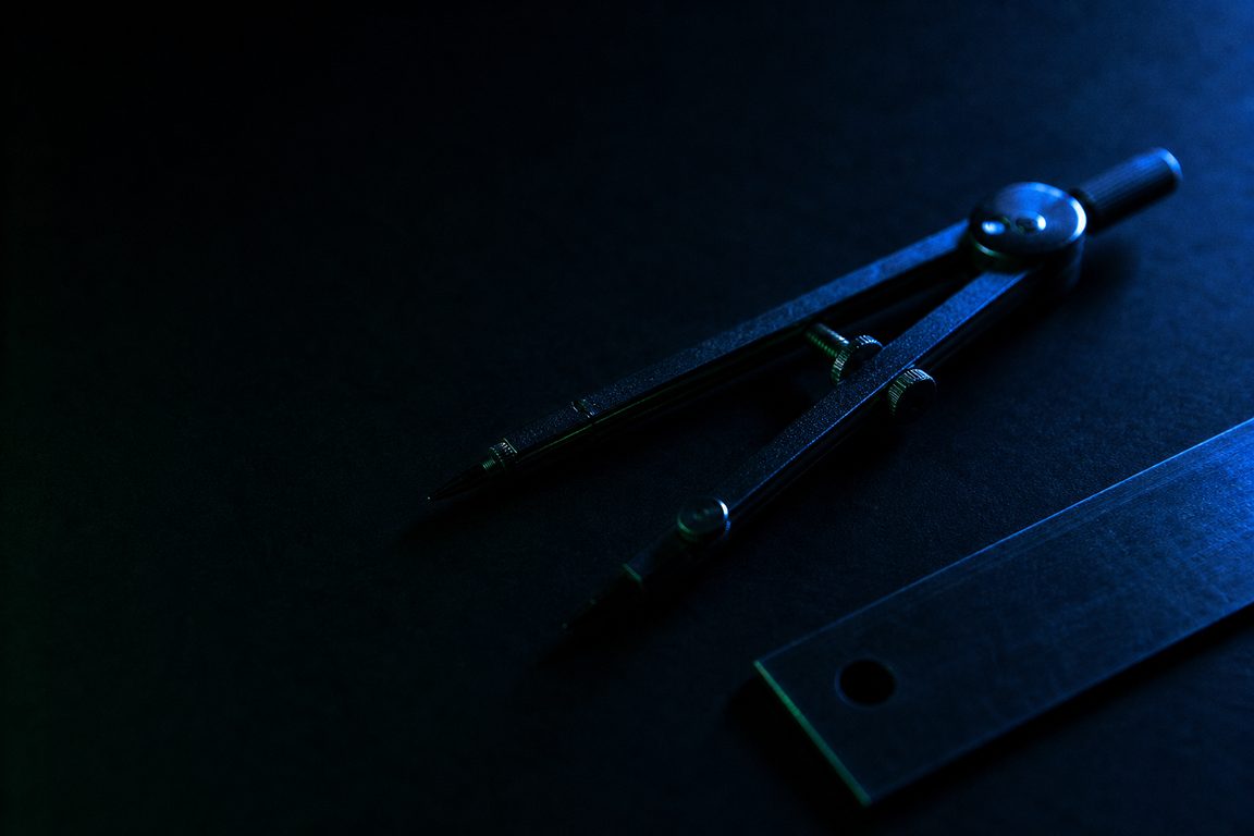 A drafting compass and straight edge on dark matte paper
